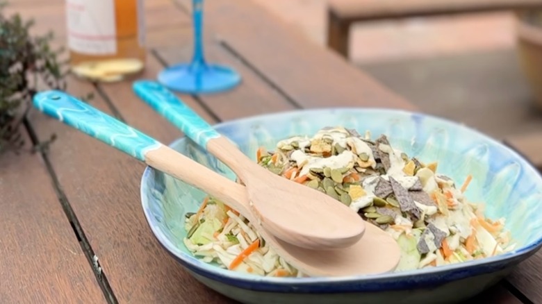 Wooden spoons with DIY blue resin handles rest in a bowl of salad on an outdoor patio table.