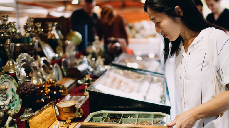 A person looking at an antique stand full of jewelry and silverware at a market.