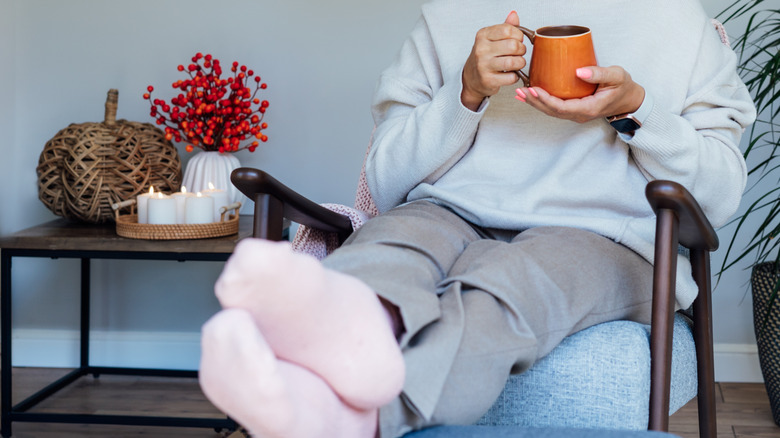 Woman sitting beside a table holding candles, a white pumpkin vase, and a woven pumpkin