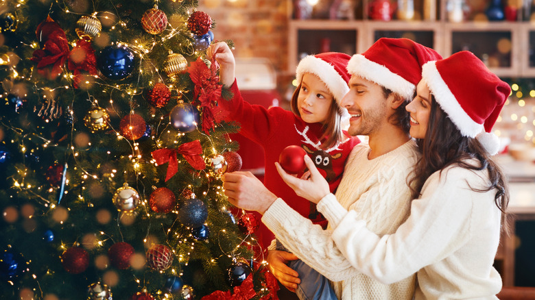 A smiling family putting ornaments on a lit Christmas tree