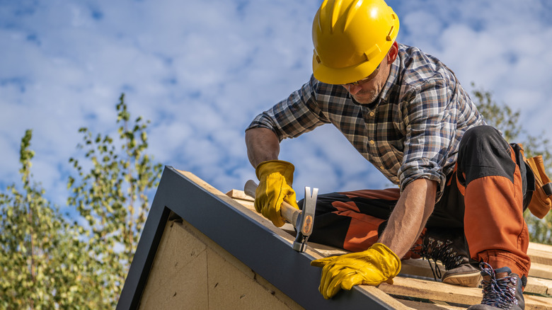 An older man wears a hard hat and gloves while installing a roof.