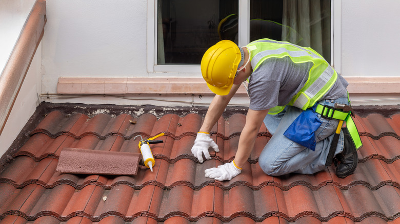 A construction worker patches red roof tiles.