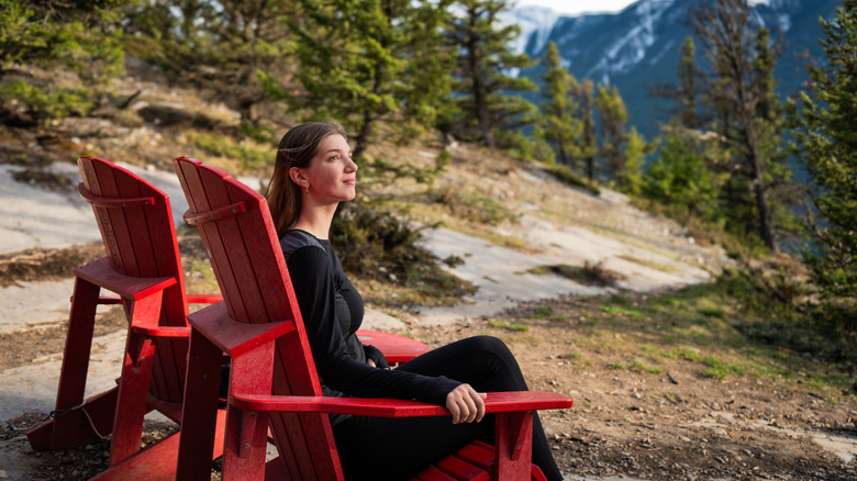 Woman sitting in one of two Adirondack chairs in the mountains