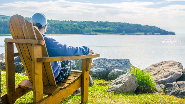 Person sitting in an Adirondack chair looking out onto a lake