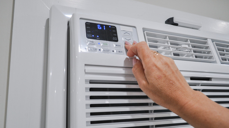 A hand adjusts the temperature on a window air conditioner.