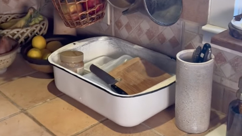 A cute white dish basin containing dirty dishes on a kitchen countertop