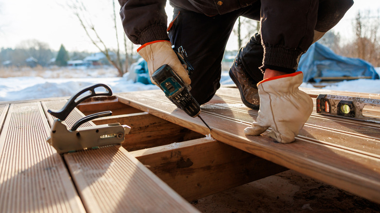 A person with a drill installing a deck surrounded by snow