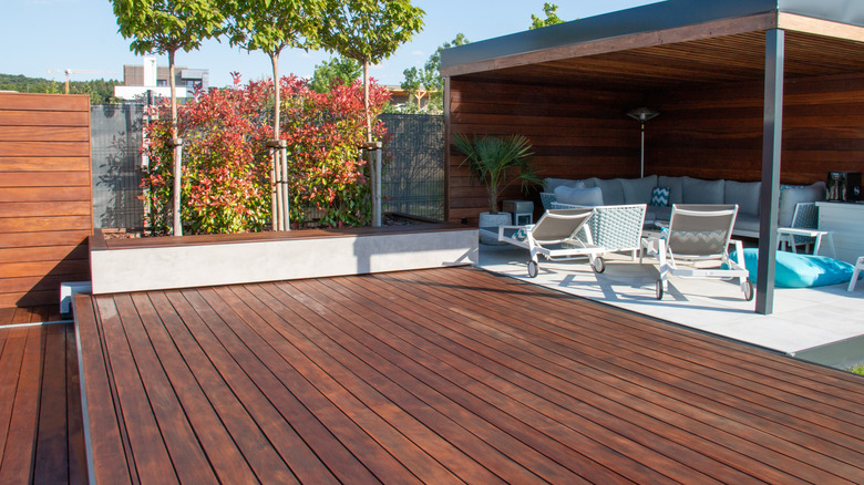A modern garden scene with a hardwood deck and patio furniture under overhang