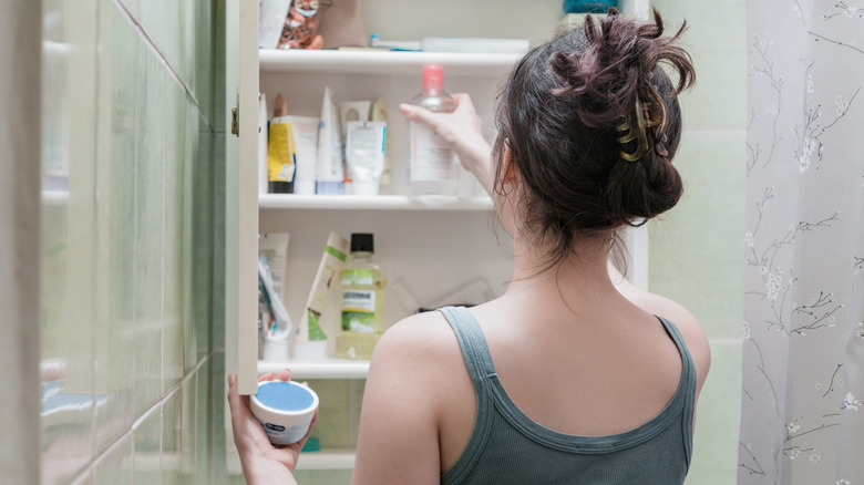 Woman grabbing hygiene products from bathroom cabinet