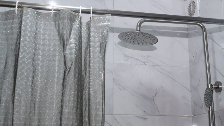 A stainless steel shower head, marble tiles, and a gray curtain.