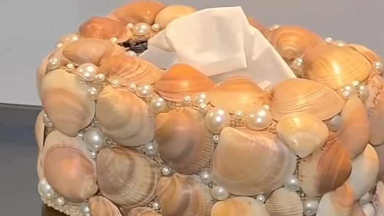 A tissue box covered in seashells and faux pearl beads.