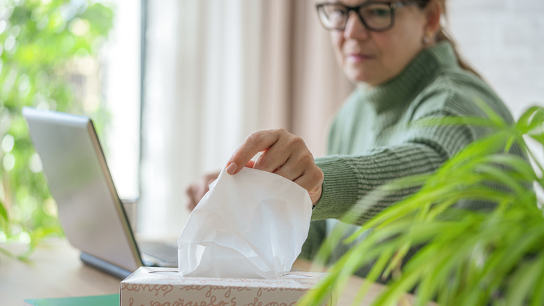 A woman reaches for a tissue from a basic tissue box.