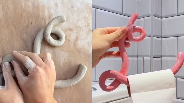 Two hands hold an L-shaped toilet paper roll holder made of clay against a white subway-tiled bathroom wall.
