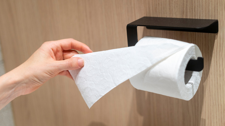 A hand pulls toilet paper off a roll in a bathroom.