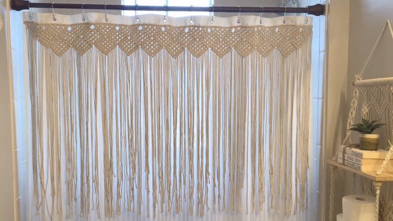 A macrame curtain hanging on a shower curtain rod with a cotton backing