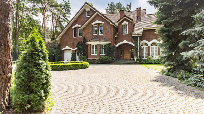 Brick paver driveway and landscaping leads to a large, red brick home