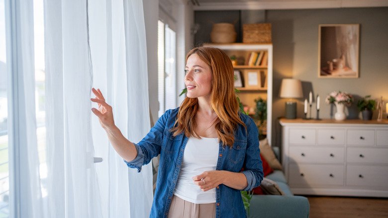 A person touches their sheer white curtains.
