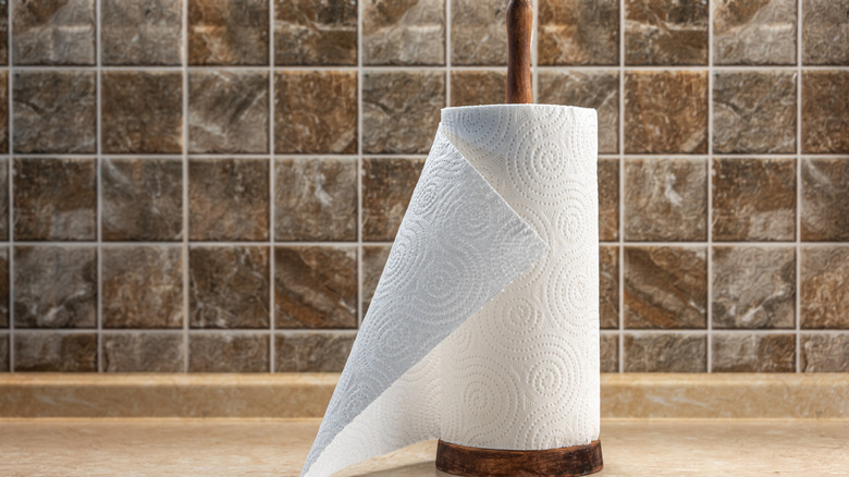 A paper towel roll on a wooden holder sits on a kitchen countertop with a tiled backsplash.