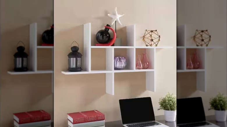 An abstract cubby-style wall shelf used to display sculptures and vases above a work desk.