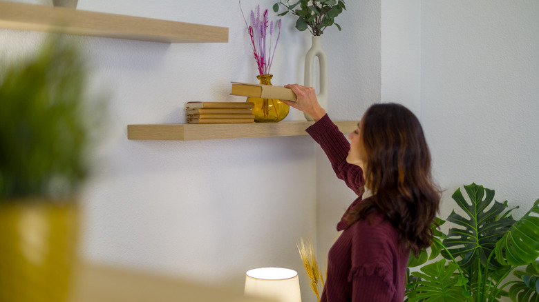 A woman putting a book on a wooden floating wall shelf.