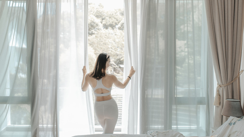 Woman opening sheer drapes in front of sliding glass doors