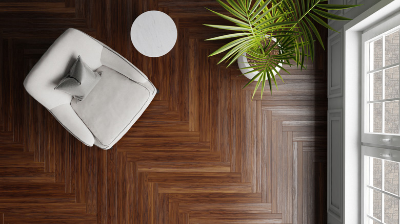 Bird's eye view of a dark herringbone patterned wooden floor with an arm chair, table, and plant