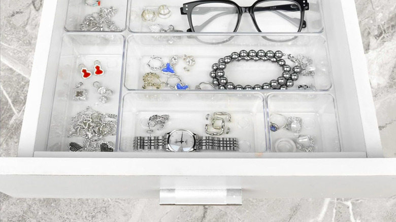 Small plastic bins in a white drawer with jewellery inside them.