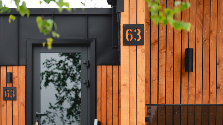 A home with natural-wood-colored siding and black accents, including lights and house number signs