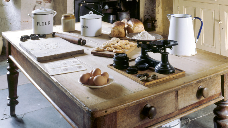 Vintage wooden work table, used for food preparation, flour, sugar, and milk jug with bread and eggs.