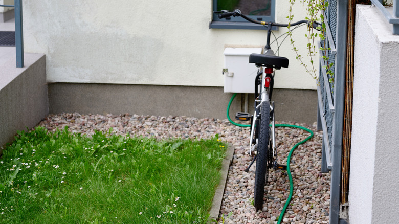 A bicycle packed on a gravel path next to a green lawn and a fence