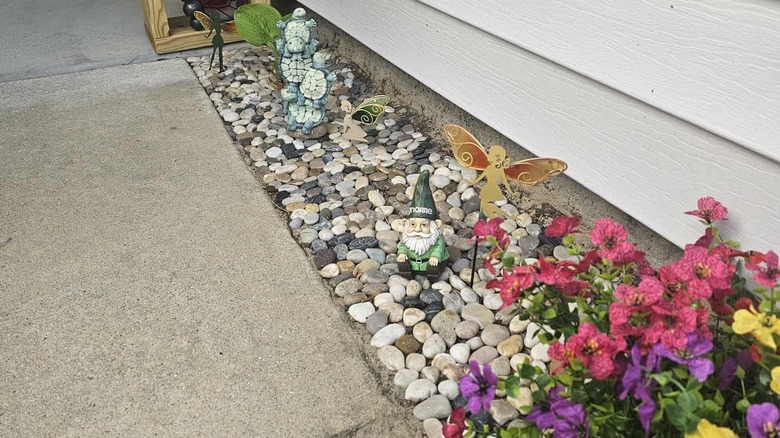 River rock stepping stones from Amazon next to a concrete pathway, with colorful flowers, garden gnomes, and fairies