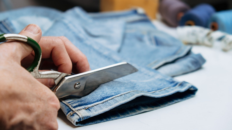 Person's hand cutting the bottom of denim jeans with a pair of scissors