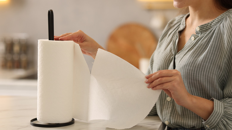 Woman tearing paper towel from roll sitting on a black paper towel holder on kitchen counter