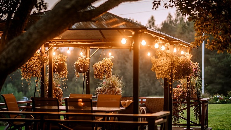 A hardtop gazebo at dusk with seating and hanging plants