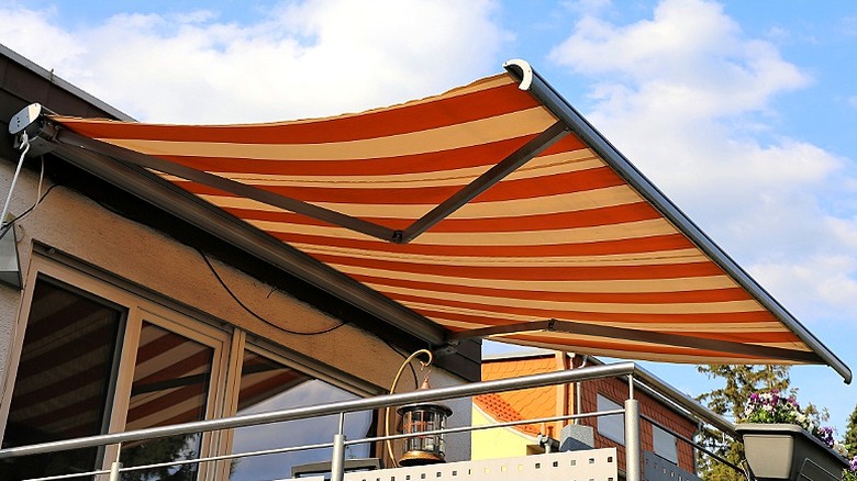 A striped retractable awning provides a patio with shade from the blue sky and clouds above