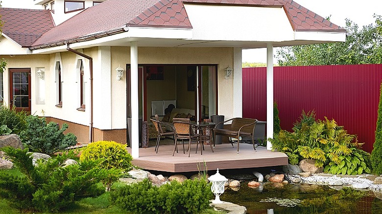 Roof extension covering the patio of a home, with a pond seen in front of the patio