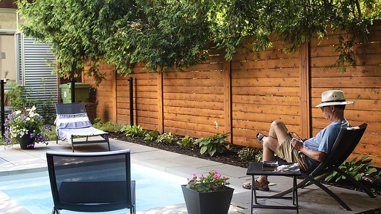 A person wearing a straw hat sits in a reclining chair outside with a nearby tree providing shade