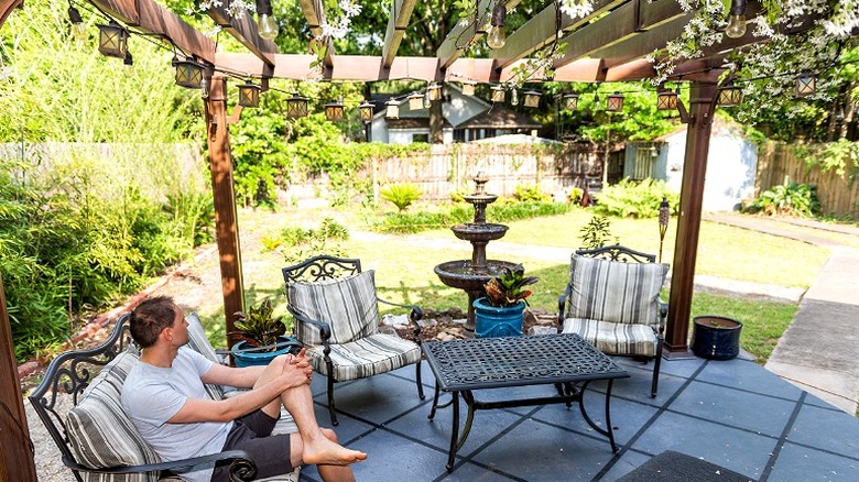 A person sits under a patio pergola in the shade