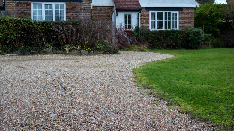 A gravel driveway and parking area in front of a brick home