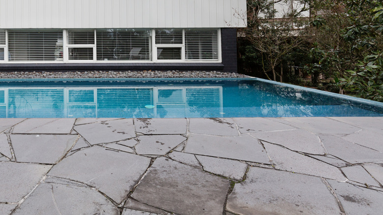 Bluestone crazy paving beside a swimming pool in the backyard of a mid-century home.
