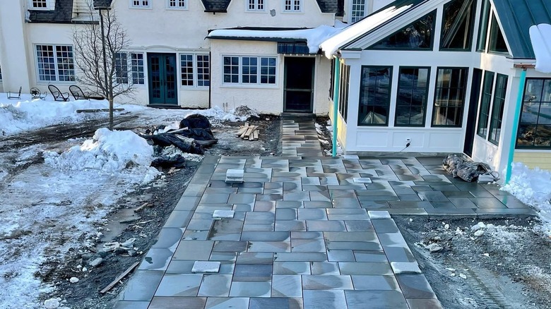A partially installed bluestone paver patio surrounded by snow.