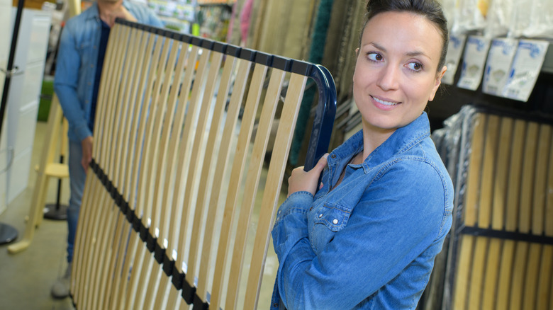 People carrying a metal bed frame with attached wooden mattress support slats.