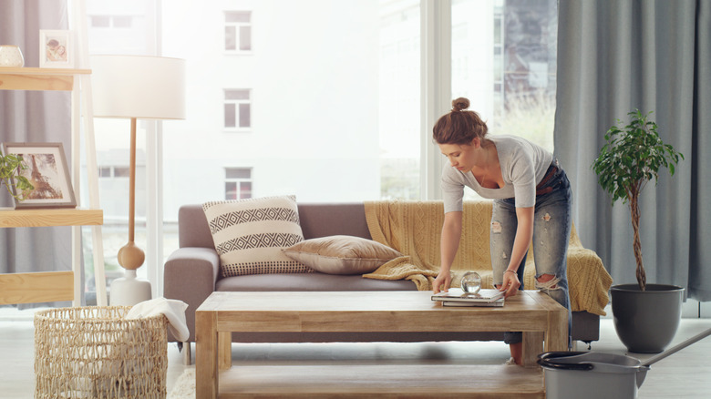 A woman adjusting items on her coffee table in front of a couch covered in blankets and pillows