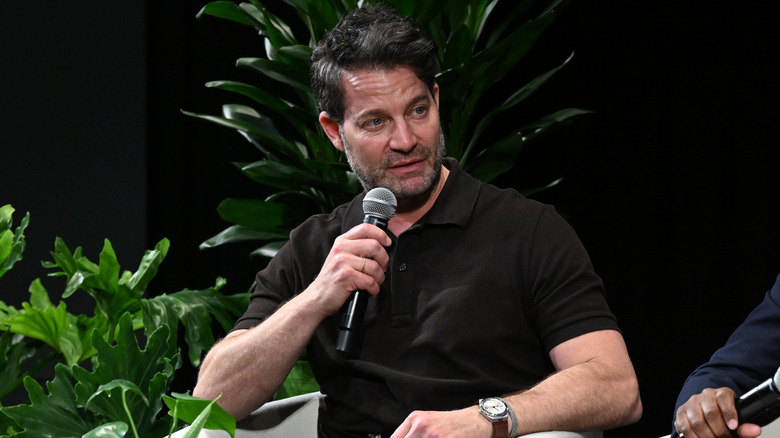 Nate Berkus speaking into a microphone with houseplants behind him.