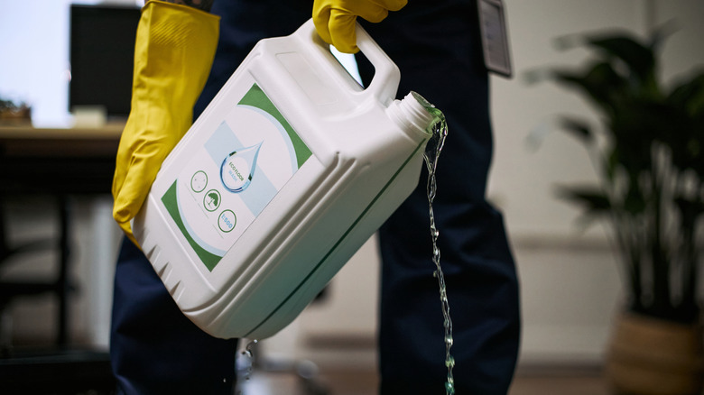 Person wearing yellow gloves pouring detergent from a white bottle.