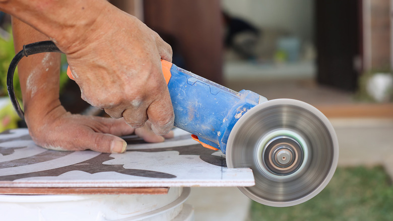 Man using an angle grinder to cut a piece of light-colored tile