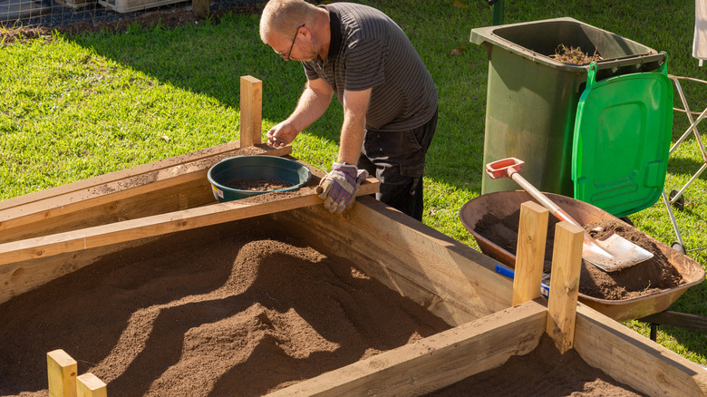 A gardener using a commercial soil sifter to sift soil for a raised garden bed
