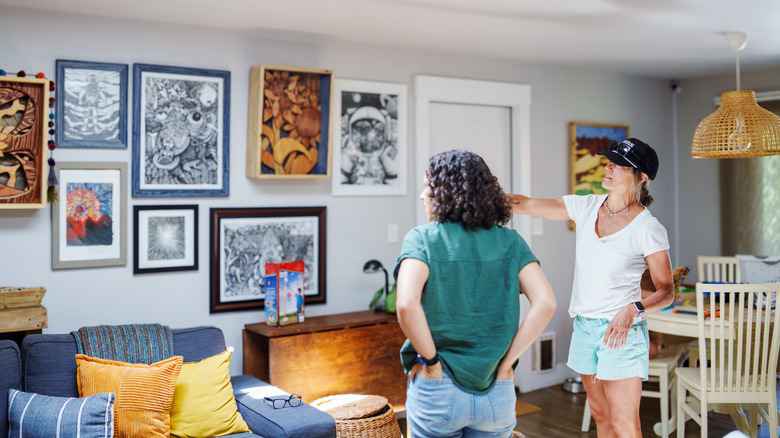 Women discussing a collage wall in the living room.