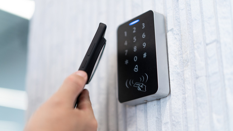 A person up a phone to a lock with a keypad to unlock a door n a white brick background