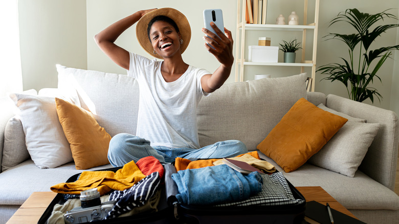 Woman packing suitcase for trip taking selfie